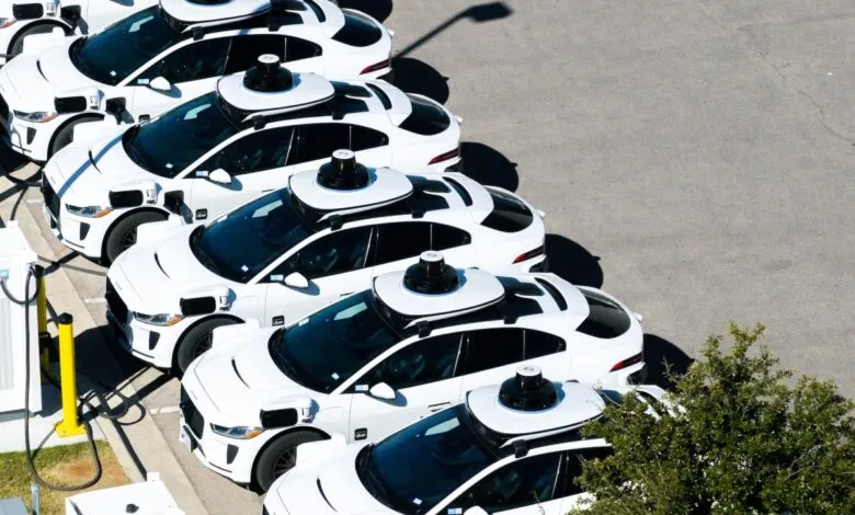 Row of white self-driving Uber vehicles charging at stations, aerial view.