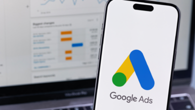 Smartphone displays Google Ads logo with laptop showing analytics in background.