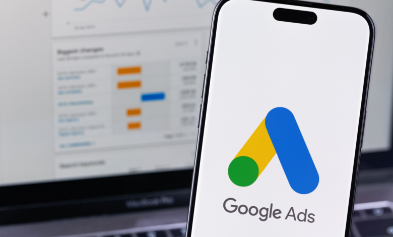 Smartphone displays Google Ads logo with laptop showing analytics in background.