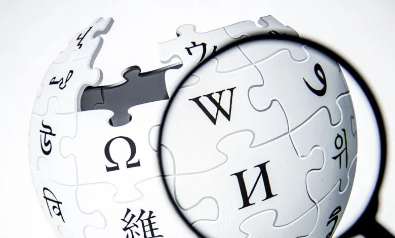 Wikipedia logo globe made of puzzle pieces, viewed through magnifying glass.