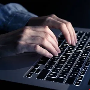 Hands typing on a backlit laptop keyboard in a dimly lit environment.