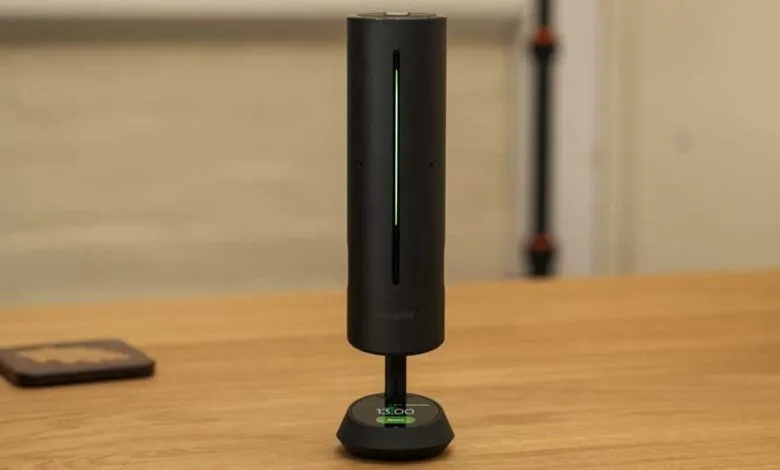 Black cylindrical device with green light on wooden surface.