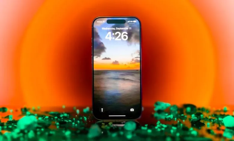 iPhone displaying sunset wallpaper, surrounded by green particles and orange background.
