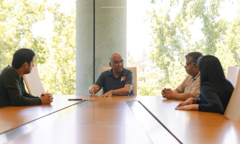 Group of four people in a meeting around a long conference table.
