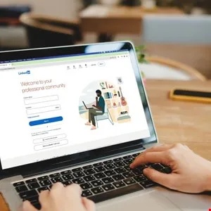 Laptop displaying LinkedIn login page with hands typing on the keyboard.