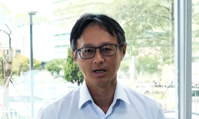 Portrait of an Asian man with glasses in front of a window.