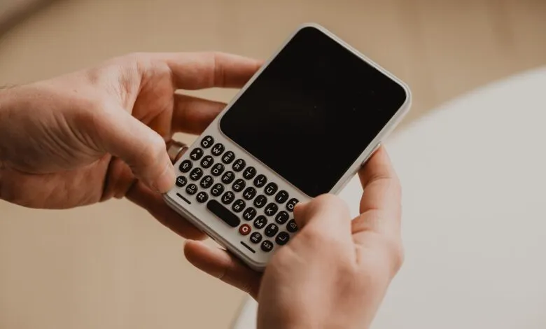 Hands holding a smartphone with a physical QWERTY keyboard.