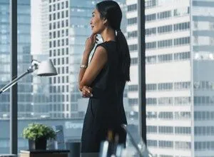 Businesswoman thoughtfully looks out office window at city skyline.