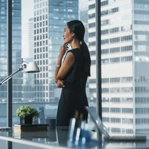 Businesswoman thoughtfully looks out office window at city skyline.
