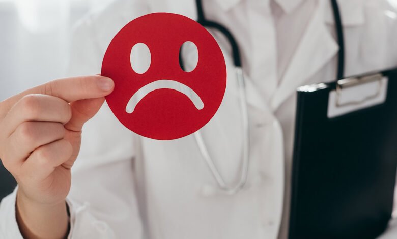 Doctor holds sad face emoticon, suggesting mental health assessment.