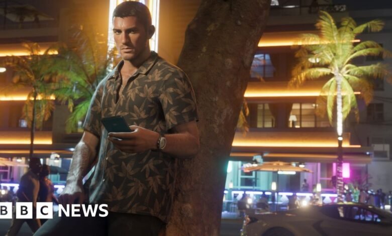 Man in tropical shirt leans against tree holding phone at night.
