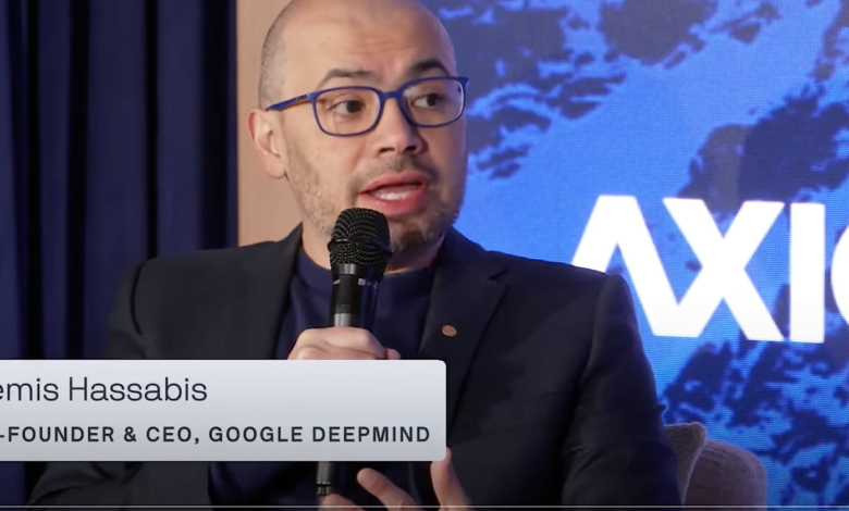 Demis Hassabis speaking at a conference, holding a microphone.