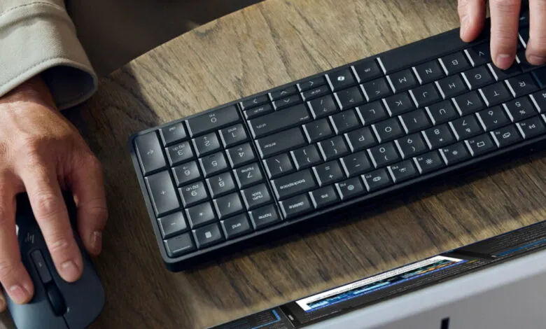 Hands using a black keyboard and mouse on a wooden desk.