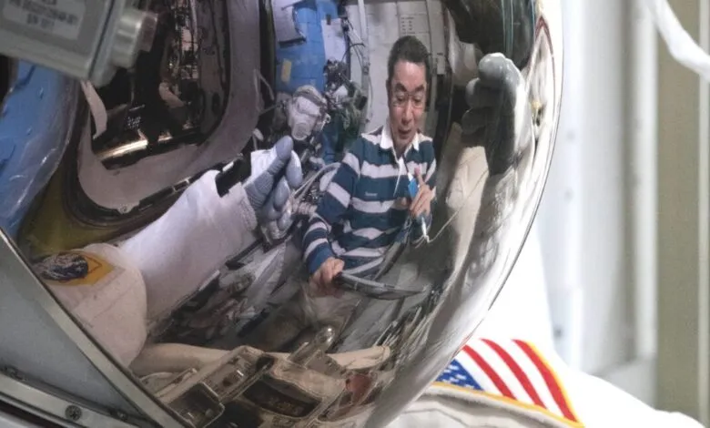 Reflection in astronaut's helmet shows crew member inside the space station.