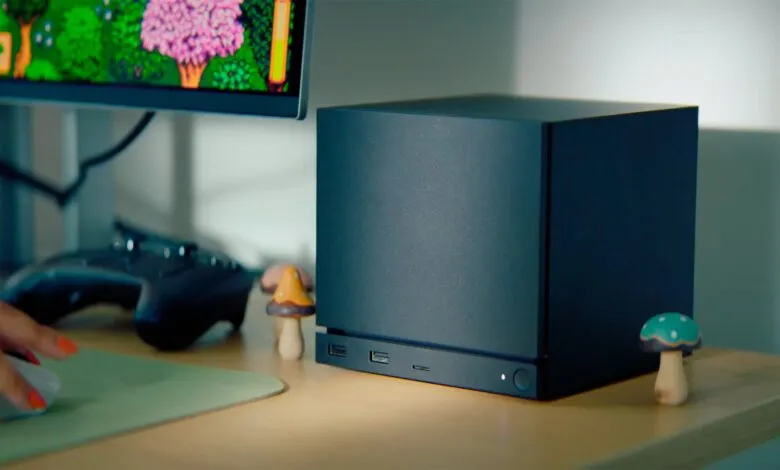 Compact black PC tower on desk with monitor and gaming controller.