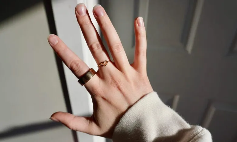 Hand with gold rings, including a heart-shaped ring, in sunlight.