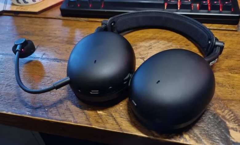 Black gaming headset with microphone on a wooden desk, keyboard in background.
