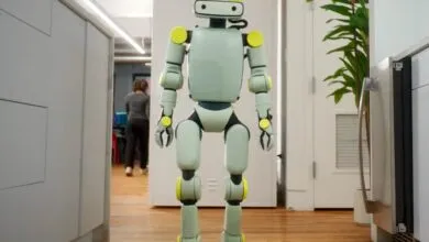 Humanoid robot stands in a modern kitchen with white cabinets and wood floors.