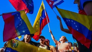 People wave Venezuelan and Cuban flags against a bright blue sky.