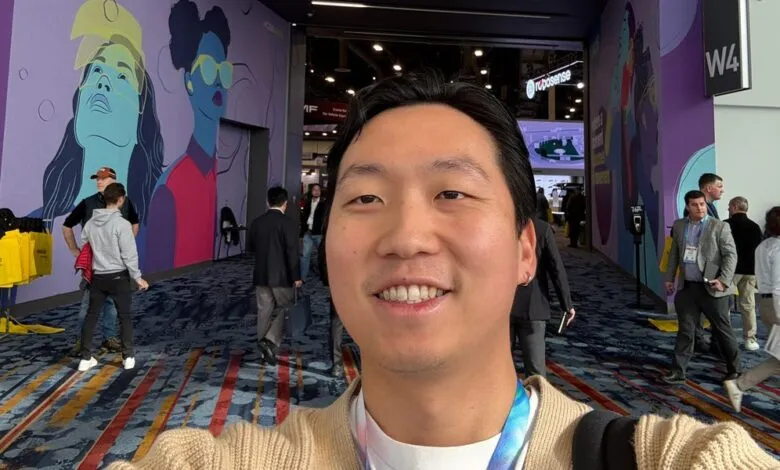 Smiling man takes selfie at a busy convention hall.
