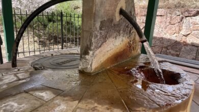 Outdoor water fountain with stone base and metal pipe pouring water.