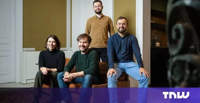Four smiling people pose indoors on a brown leather couch.