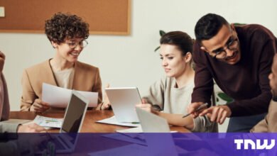 Diverse team collaborates around a table with laptops and tablets.