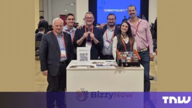 Group of six people stand behind BizzyNow booth at conference.