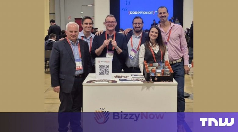 Group of six people stand behind BizzyNow booth at conference.