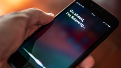 Hand holding iPhone with Siri activated, displaying 'Go ahead, I'm listening...'