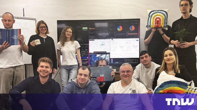 Group of ten people posing in front of a large monitor displaying data visualizations.