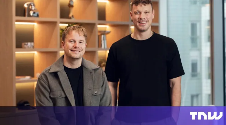 Two smiling men pose in front of a modern office setting.