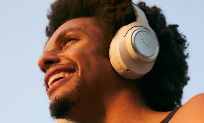 Smiling man wearing Fender headphones looking up against a blue sky.