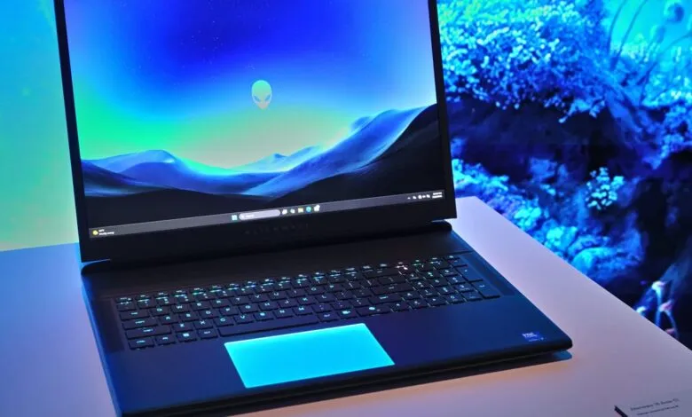 Alienware laptop with blue backlit keyboard and alien head logo on screen.