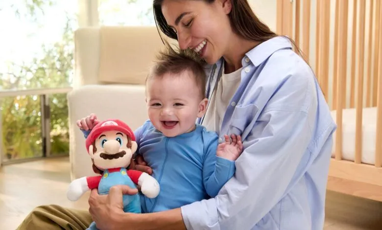 Smiling baby in mother's arms holds a plush Mario toy.