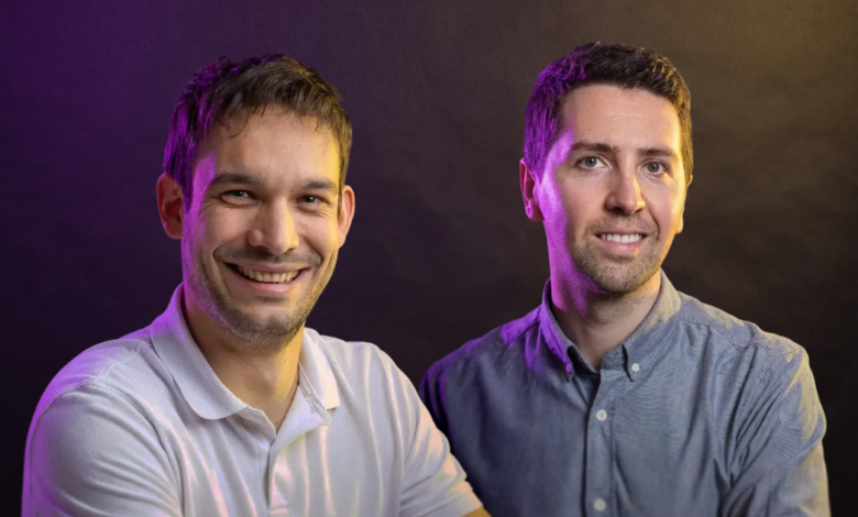 Two smiling men pose against a dark, colorful backdrop.