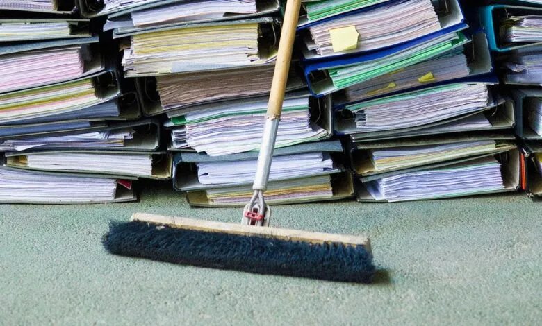Pile of overflowing file folders with a broom in the foreground.