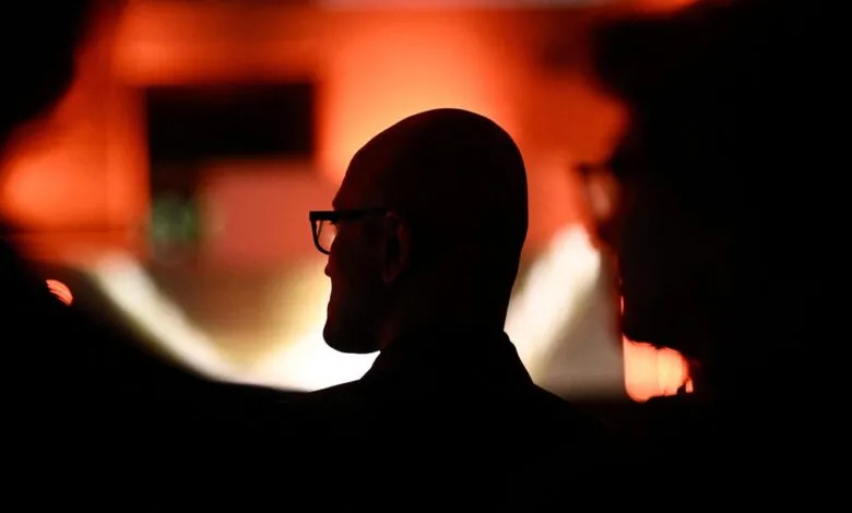 Silhouette of bald man with glasses against a red background.