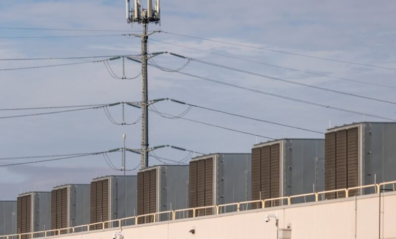 Row of HVAC units on building roof with cell tower behind.
