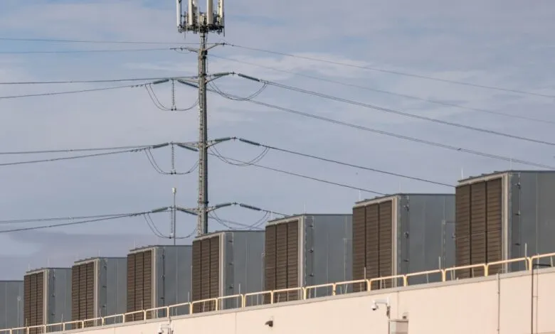 Row of HVAC units on building roof with cell tower behind.