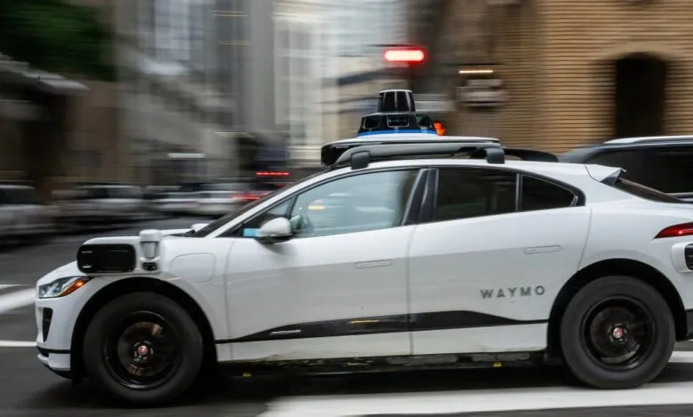 White Waymo self-driving car driving on city street.