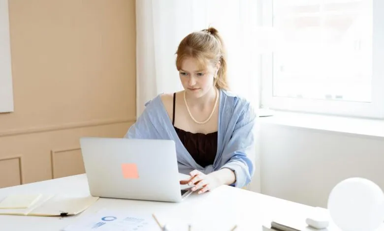 Woman with red hair working on a laptop at a white desk.