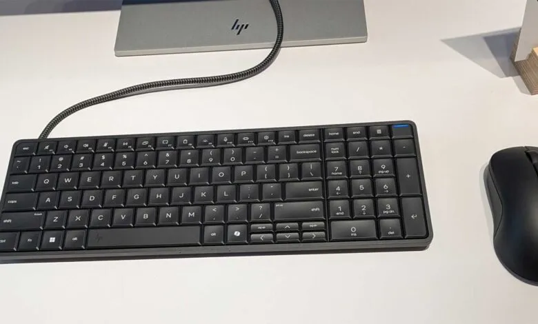HP keyboard and mouse on a white desk, monitor in background.