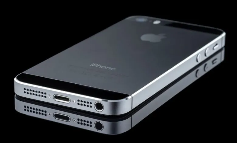 Sleek gray iPhone 5S laying on a reflective black surface.