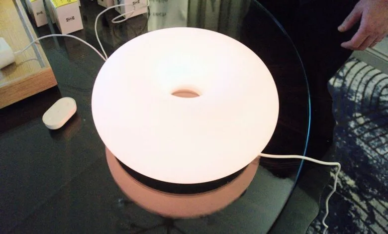 IKEA Varmblixt donut-shaped lamp on a glass table, glowing white.