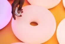 Hand holding smart home device near donut-shaped lights.