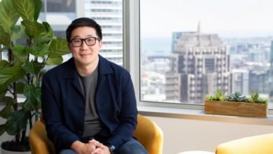 Man in glasses sits in yellow chair with city view behind him.