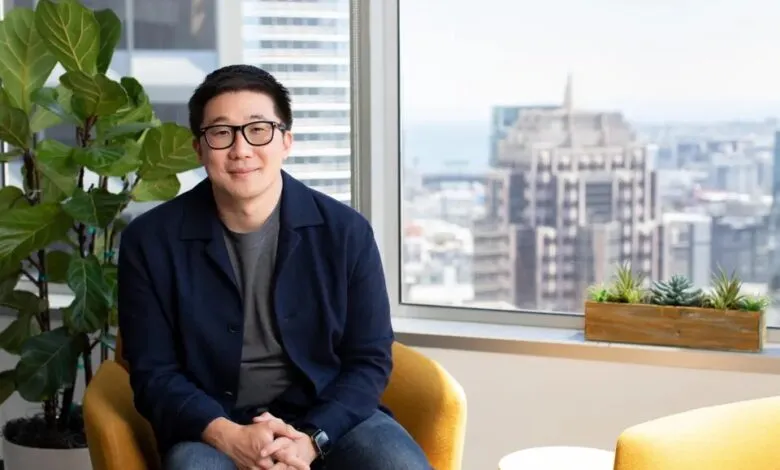 Man in glasses sits in yellow chair with city view behind him.
