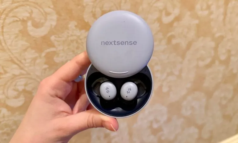 Hand holds open Nextsense wireless earbuds case with earbuds inside.