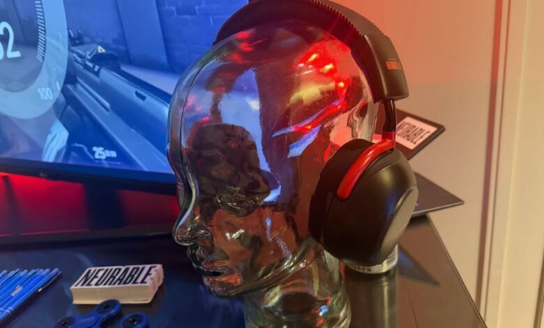 Black and red headphones displayed on a glass head, gaming monitor in background.